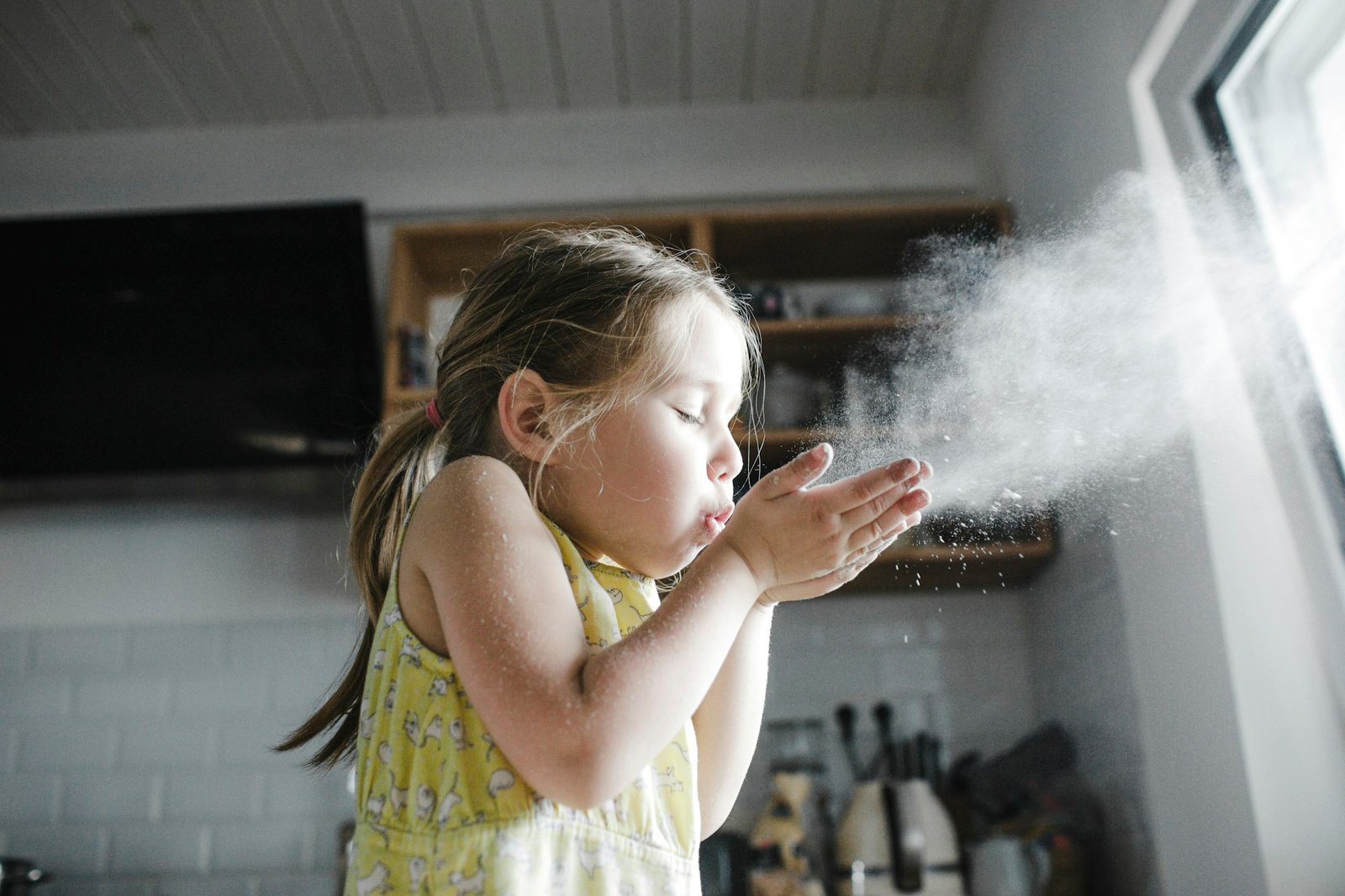 Little girl blowing flour in the air in the kitchen